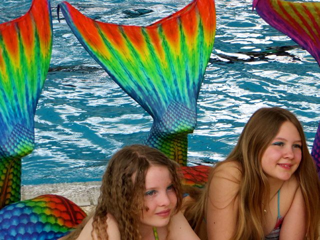 Mädchen mit Meerjungfrauflossen am Beckenrand